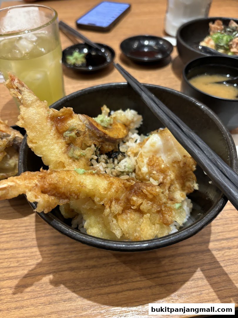 A close-up of a delicious tempura donburi dish with a side of miso soup and a drink.