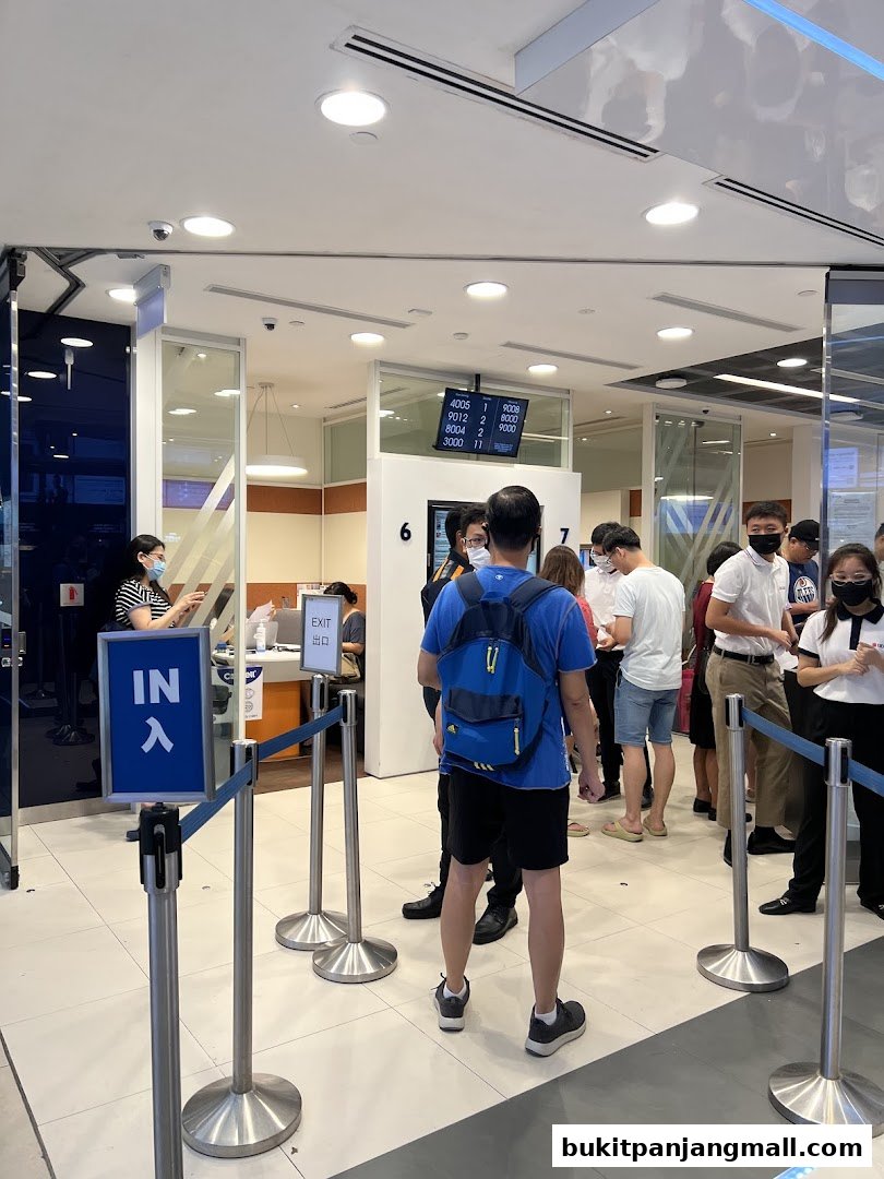People queuing inside a UOB bank branch with a digital display showing queue numbers.