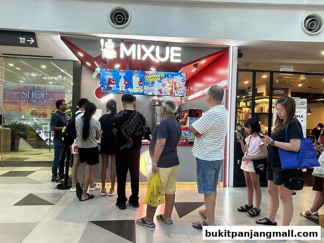A line of customers waits outside a brightly lit MIXUE ice cream and beverage shop.