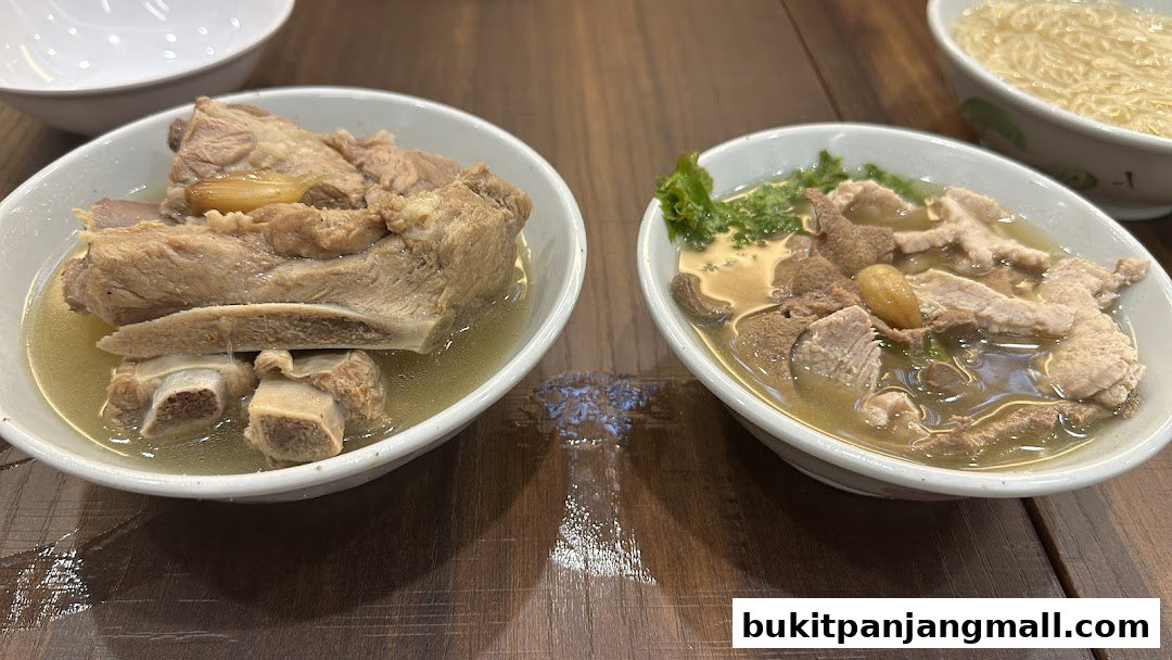 Two bowls of savory bak kut teh with tender pork ribs and offal, served with noodles.