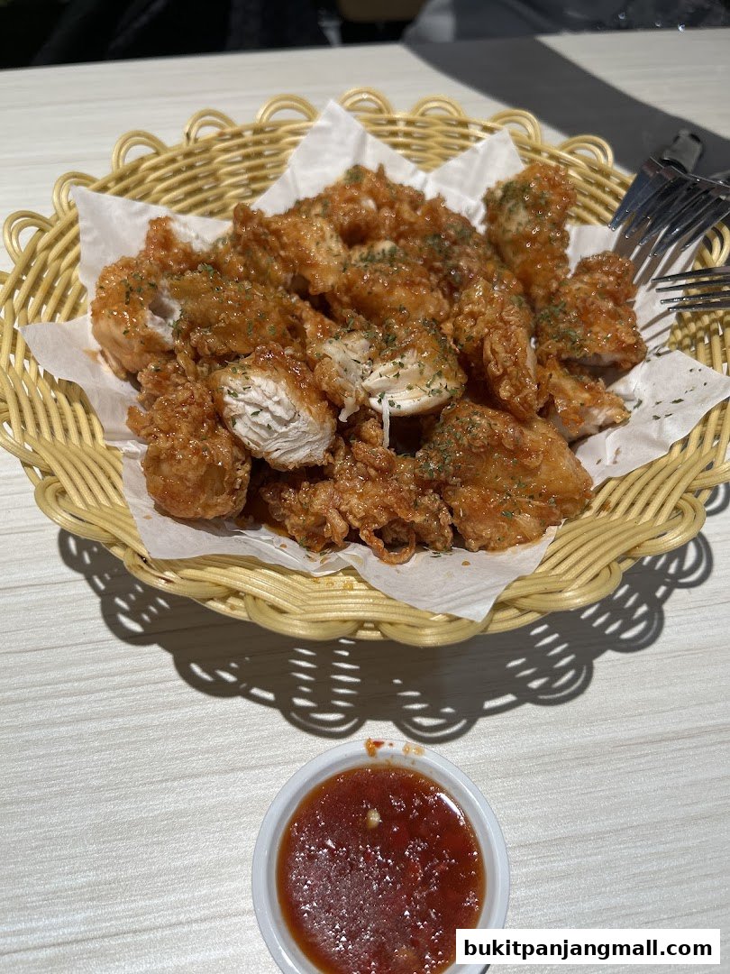 A basket of crispy fried chicken pieces coated in a glossy sauce, served with a side of dipping sauce.