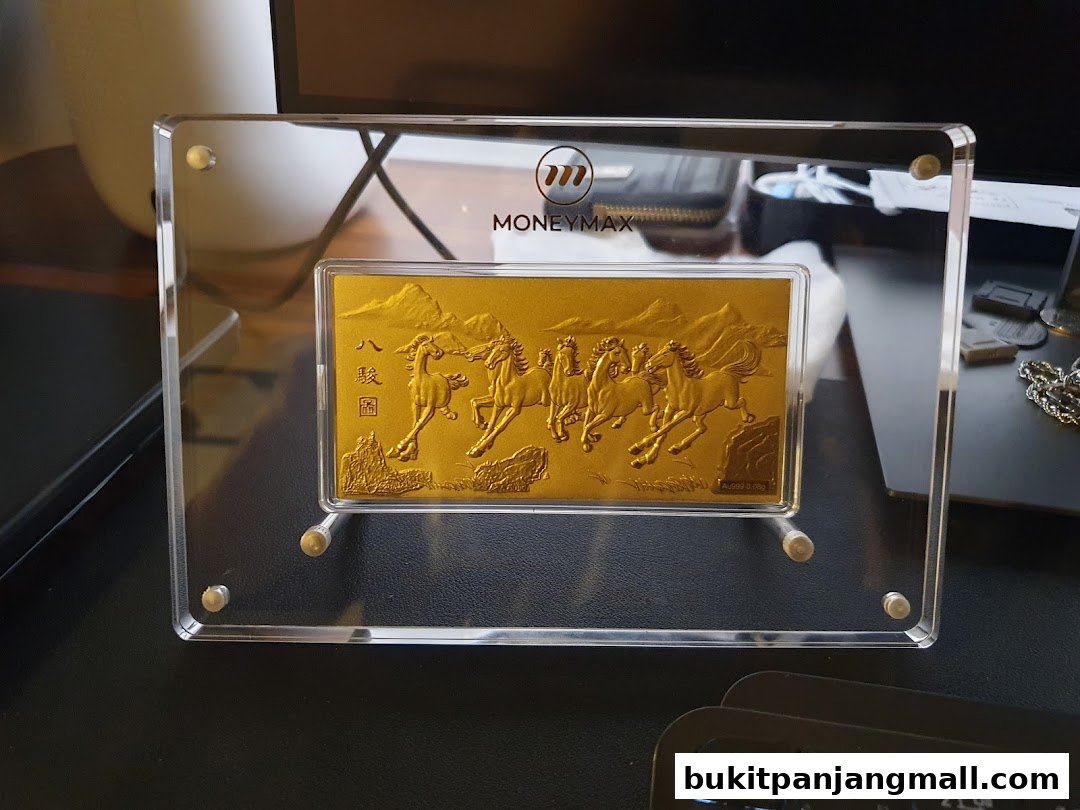 A gold bar with horses embossed, displayed in a clear acrylic frame with the MoneyMax logo.