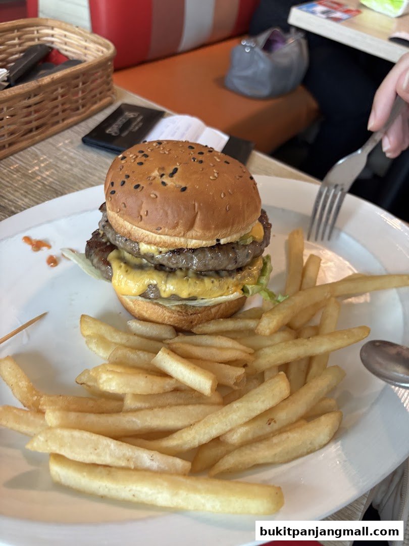 A double patty cheeseburger with fries on a white plate, with a fork and napkin in the background.