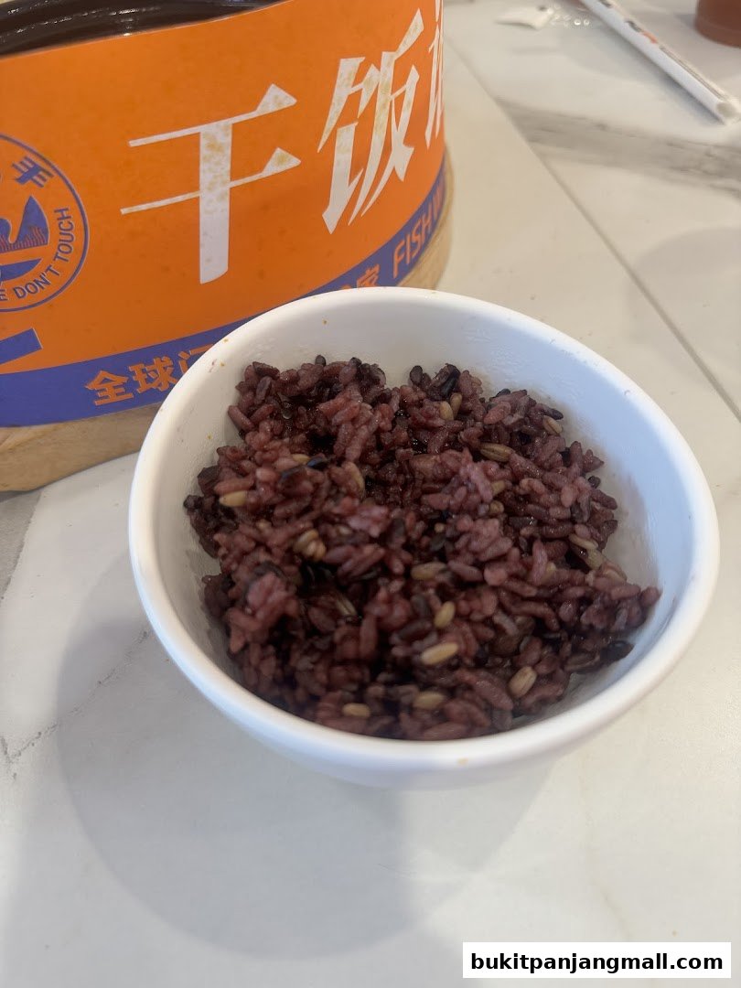 A bowl of purple rice sits in front of a large orange container with Chinese characters.