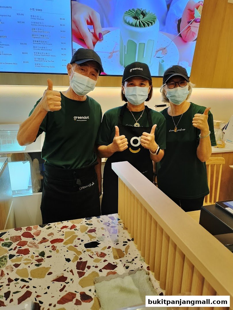 Three Greendot staff members give a thumbs up in front of a menu display.