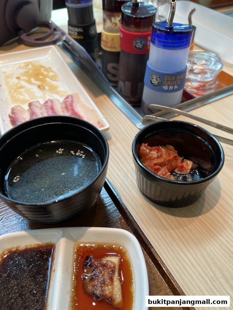 A close-up of a table setting at Yakiniku Like, featuring grilled meat, kimchi, and sauces.