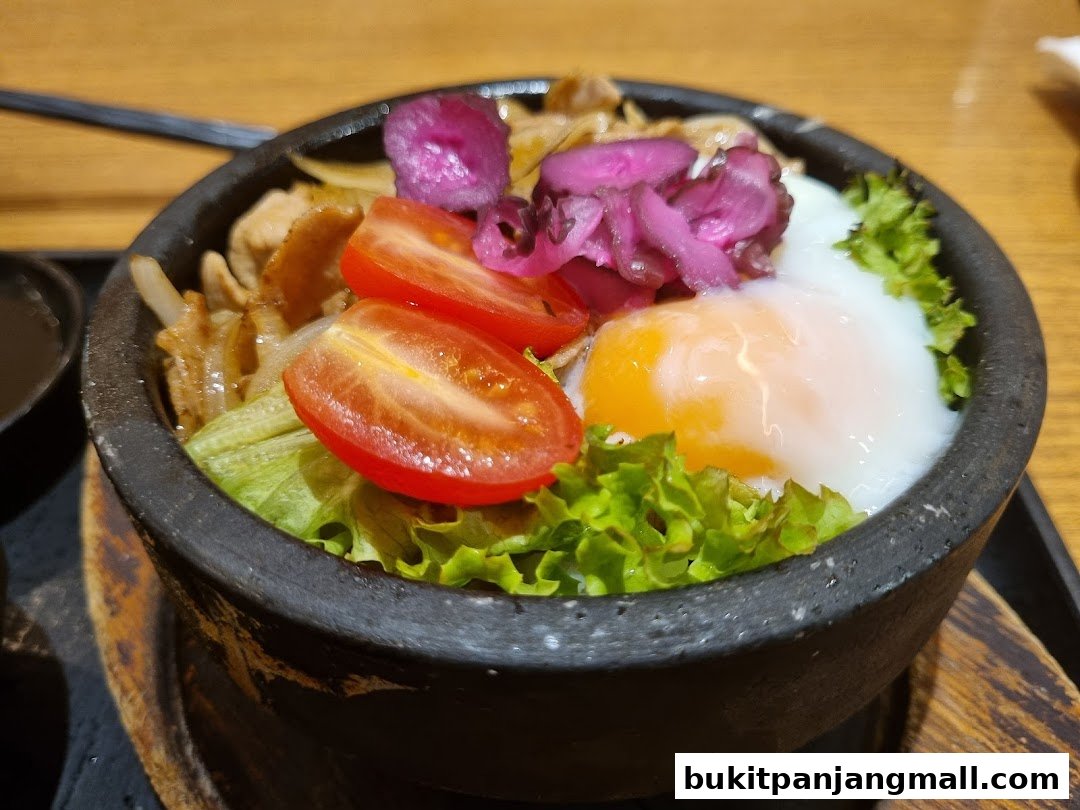 A close-up of a stone bowl filled with rice, meat, vegetables, and a fried egg.