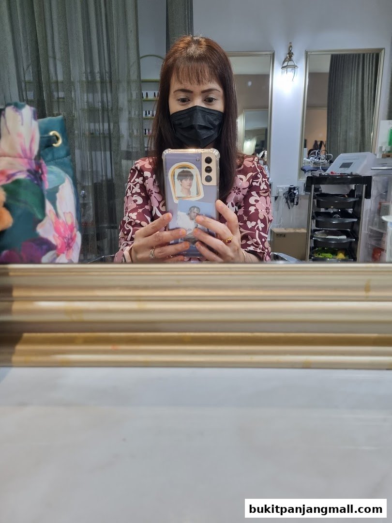 A woman in a mask takes a selfie in a salon, holding a phone with stickers.