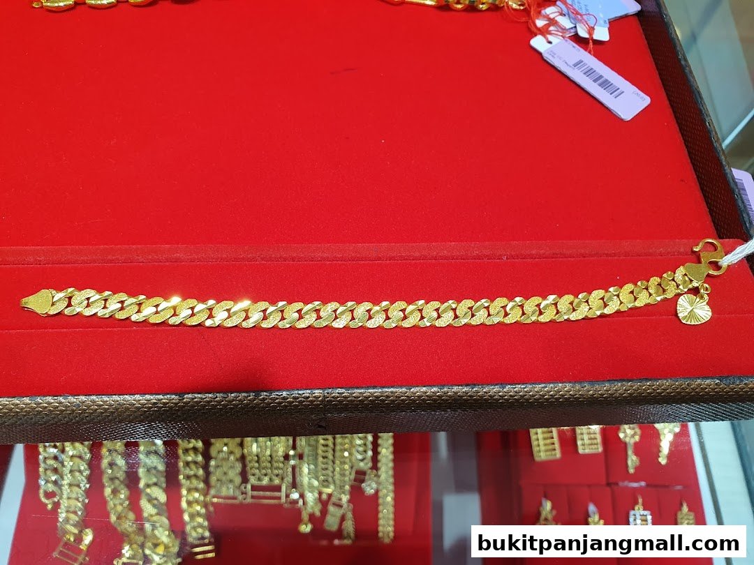 A close-up of a gold bracelet with a textured curb chain and a small charm.