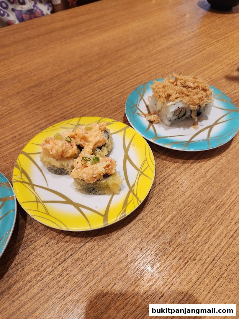 Two plates of sushi rolls with toppings sit on a wooden table.