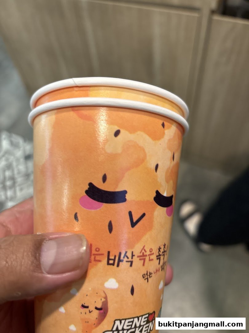 A hand holds a NeNe Chicken cup with a cute cartoon design and Korean text.