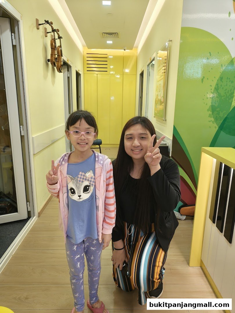 Two smiling girls pose in a bright hallway with musical instruments and colorful decor.