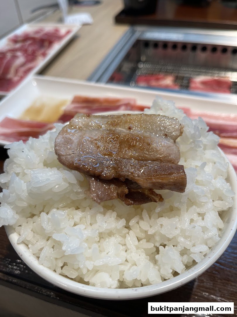 A close-up of grilled pork belly served on a bed of fluffy white rice.