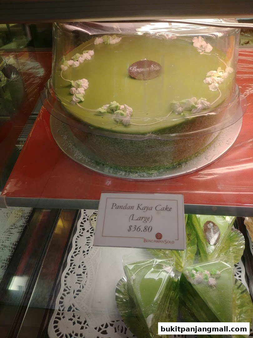 A large Pandan Kaya Cake is displayed in a clear plastic container with decorative frosting.