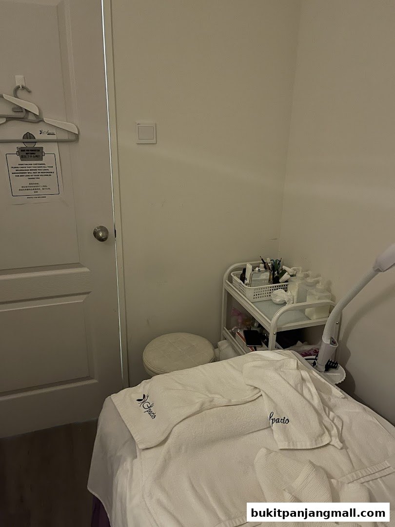 A treatment room with a massage bed, stool, and trolley with supplies.