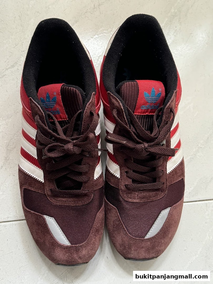A pair of maroon and white Adidas sneakers with dark brown laces.