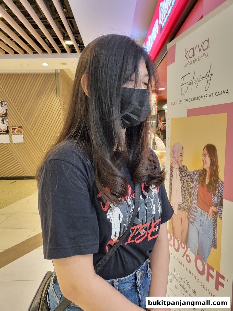 A woman wearing a mask stands next to a promotional banner for Karva Salon.