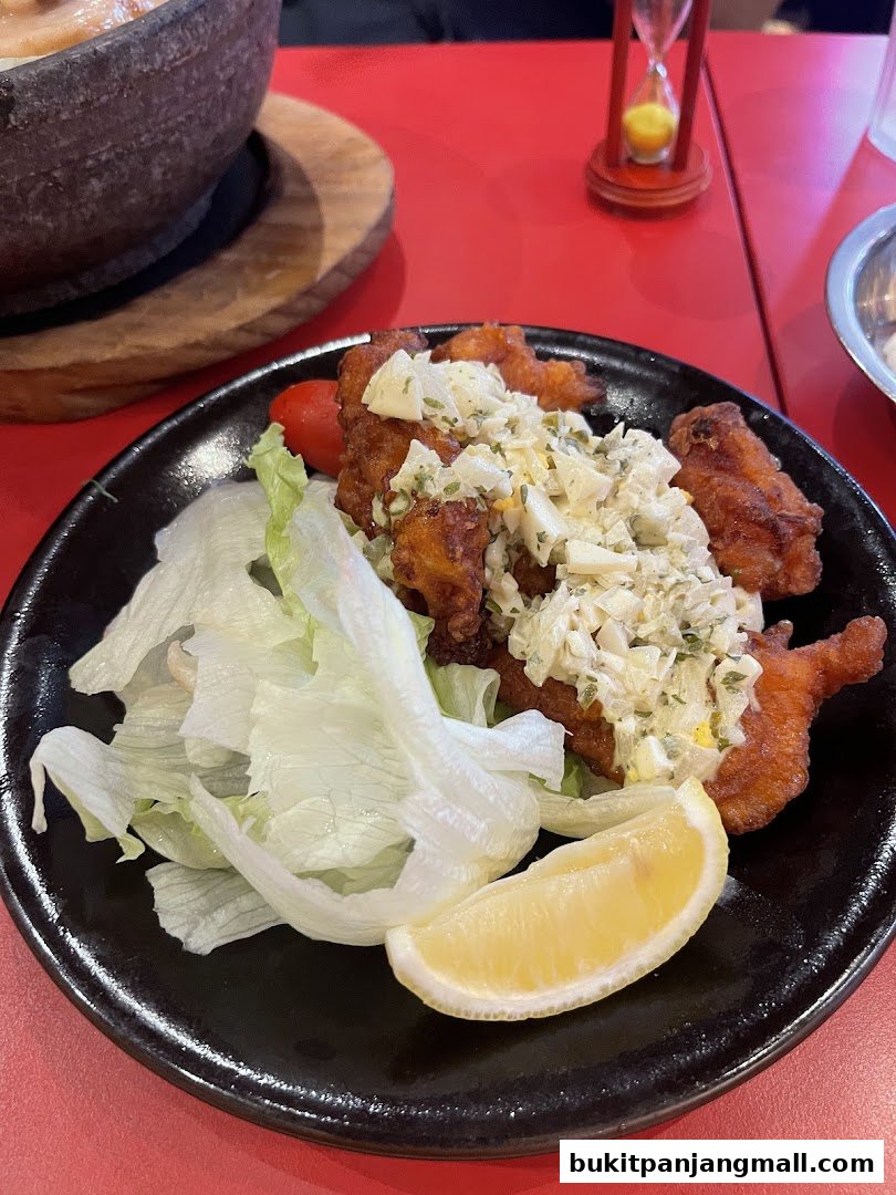 A plate of crispy fried chicken with tartar sauce, lettuce, tomato, and lemon.