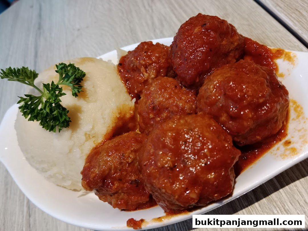 A plate of meatballs in tomato sauce served with mashed potatoes and parsley.