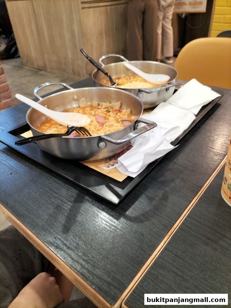 Two steaming pots of Korean ramen with sausages and vegetables on a table.
