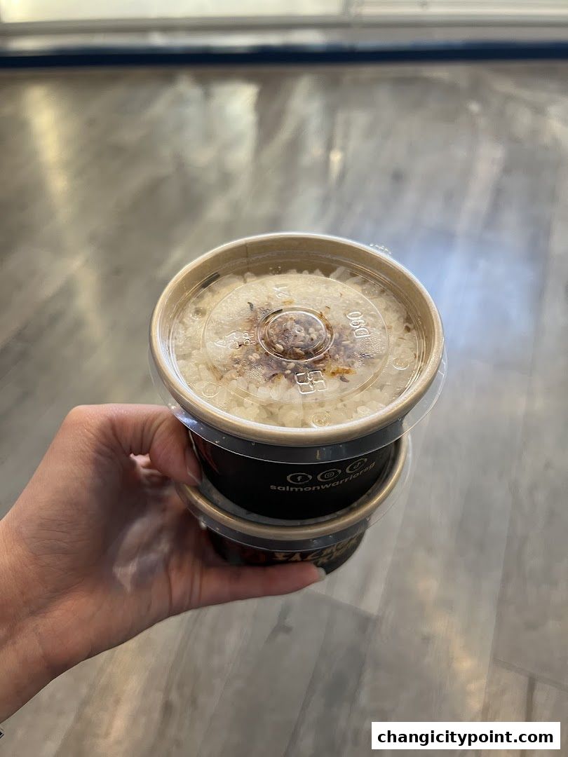 A hand holds two takeaway containers of rice from Salmon Warrior Express.