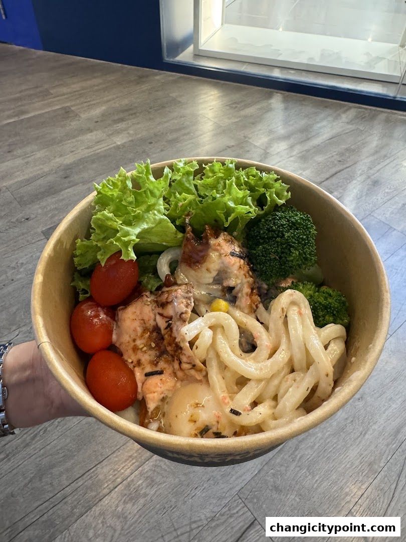 A close-up of a salmon bowl with udon noodles, vegetables, and cherry tomatoes.