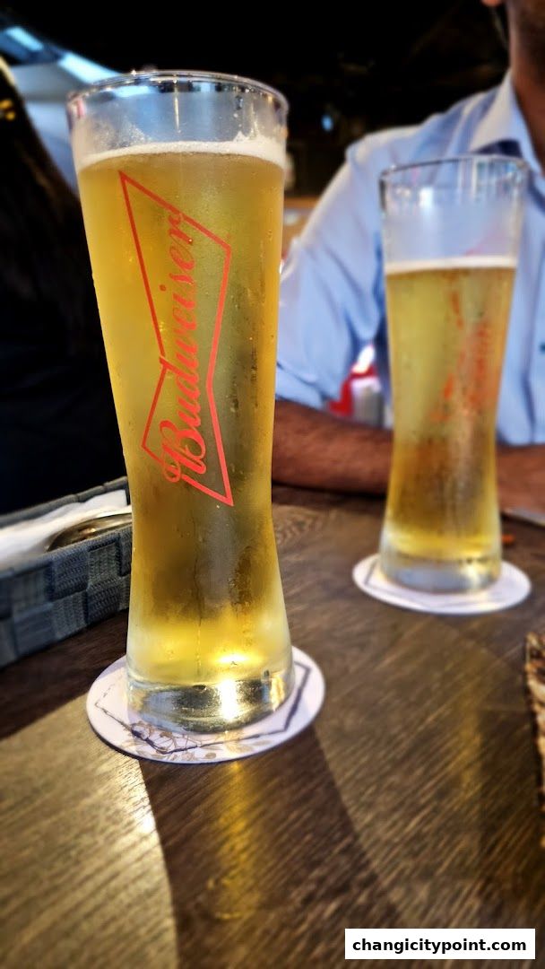 Two tall glasses of cold Budweiser beer on a wooden table.