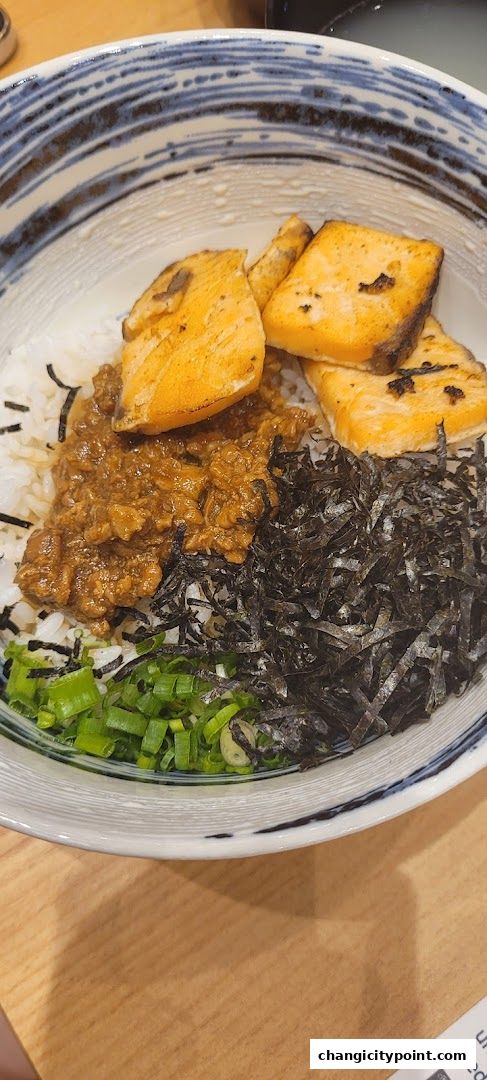 A close-up of a bowl of rice topped with grilled salmon, minced meat, seaweed, and scallions.