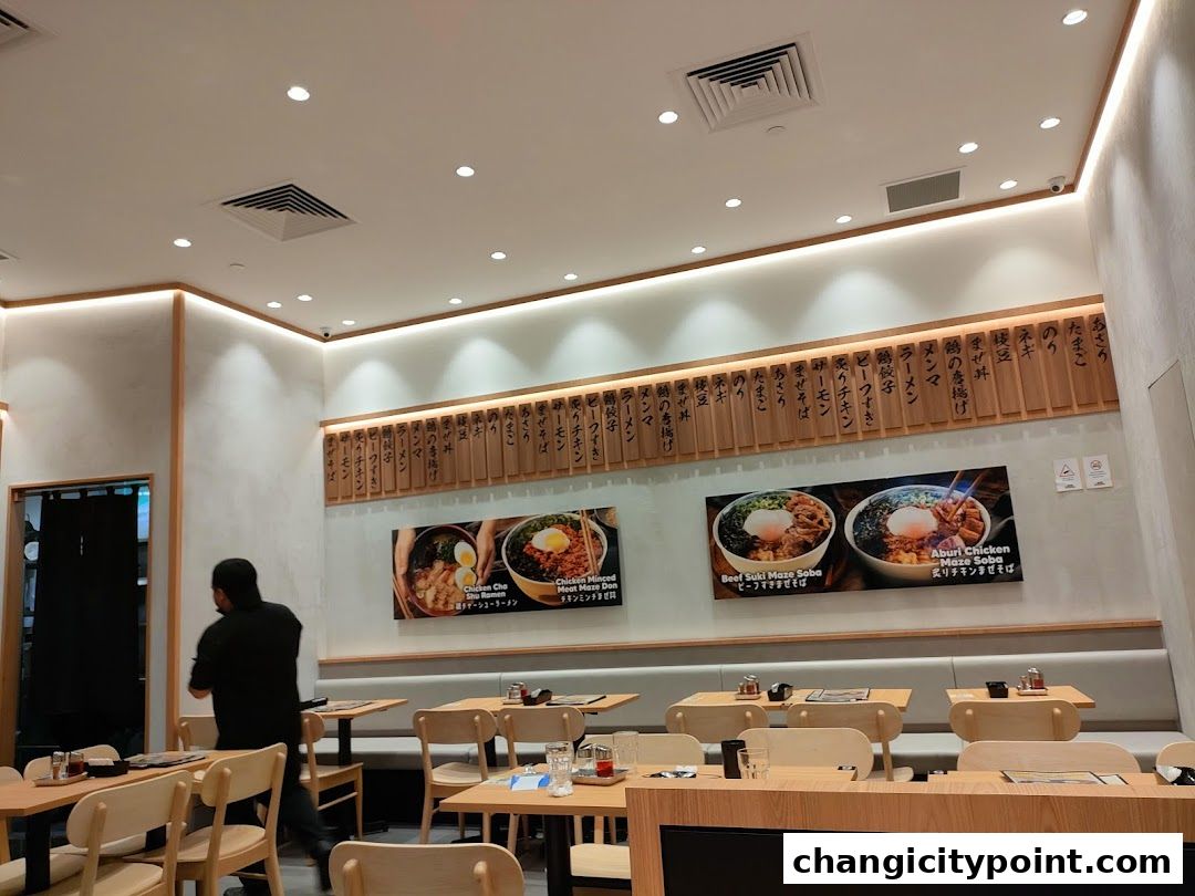 Interior of a Japanese restaurant with tables, chairs, and food images on the wall.
