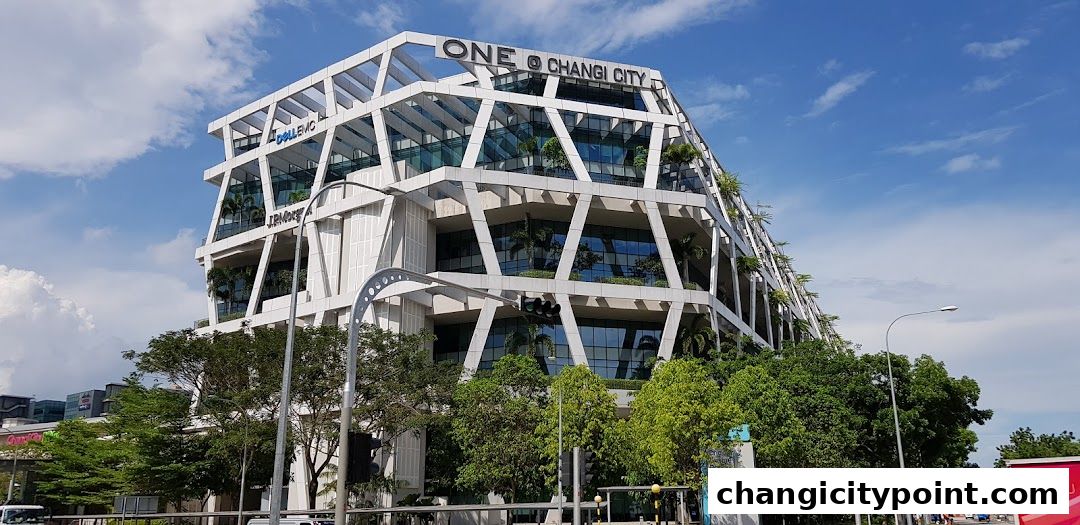 Modern office building with geometric facade and lush greenery, under a blue sky.