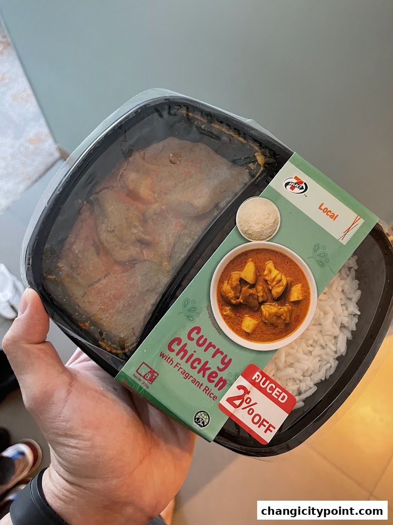 A hand holds a 7-Eleven meal of curry chicken with fragrant rice, offering a 2% discount.