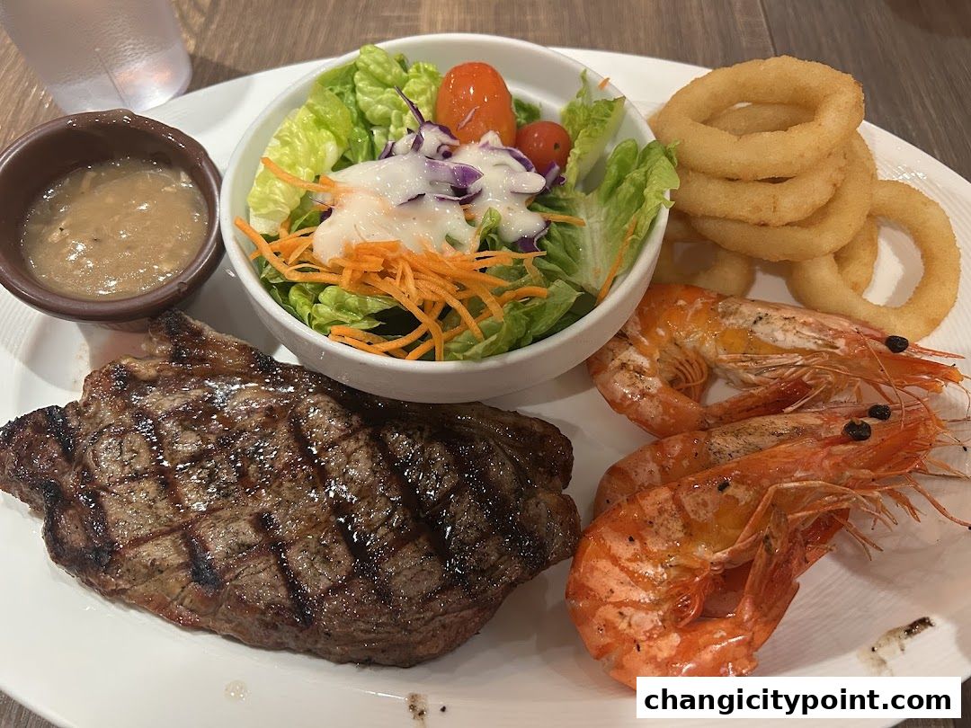 A grilled steak with prawns, salad, onion rings, and sauce on a white plate.