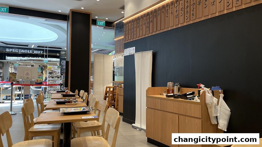 Interior of a Japanese restaurant with wooden tables, chairs, and Japanese text on the wall.