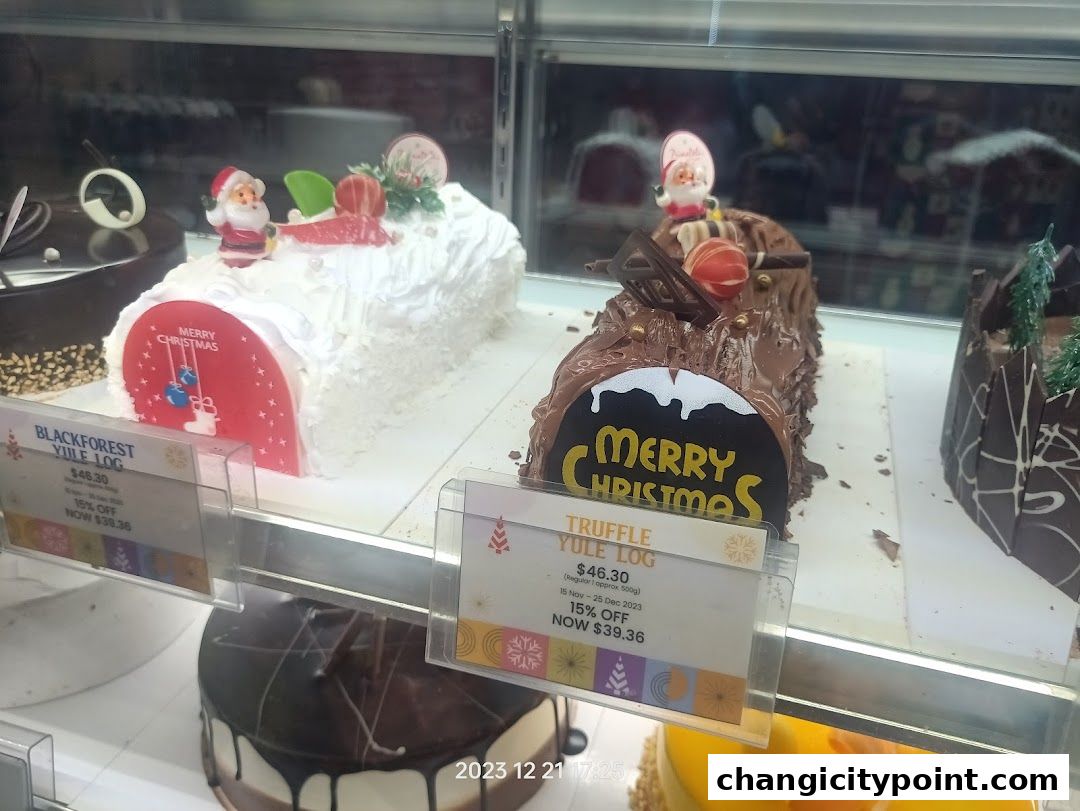 Christmas log cakes displayed in a bakery case, featuring festive decorations and pricing.