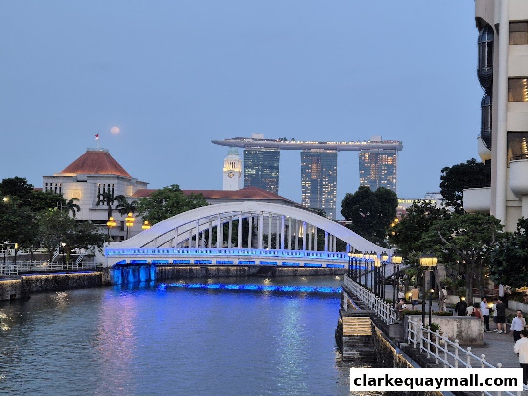 Singapore River at dusk with illuminated bridge and Marina Bay Sands in the background.