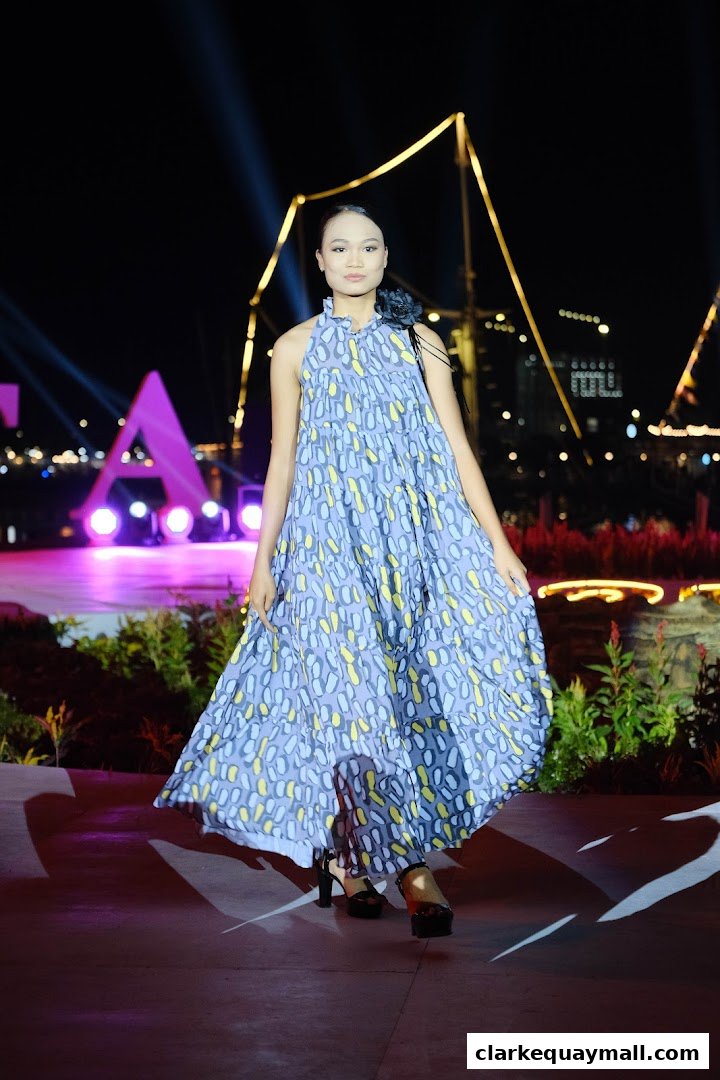 A model walks on a runway at night wearing a patterned dress and high heels.