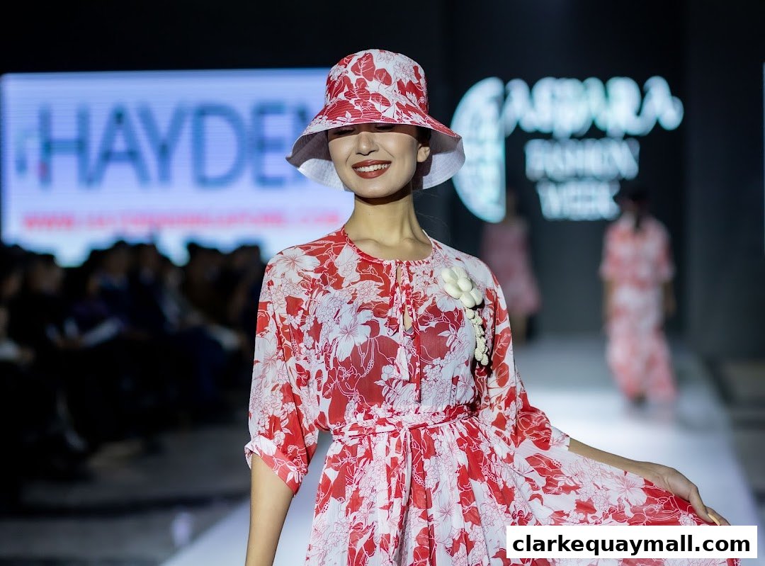 A model wearing a red and white floral dress and hat on a runway.