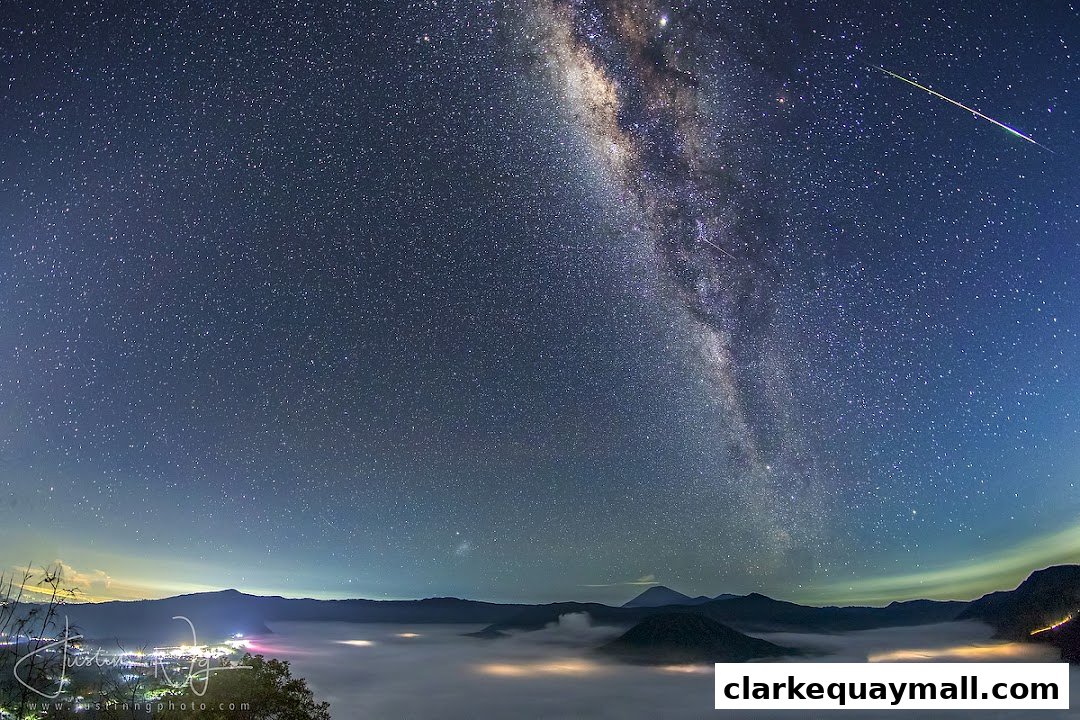A breathtaking view of the Milky Way galaxy over a misty landscape with mountains and distant lights.