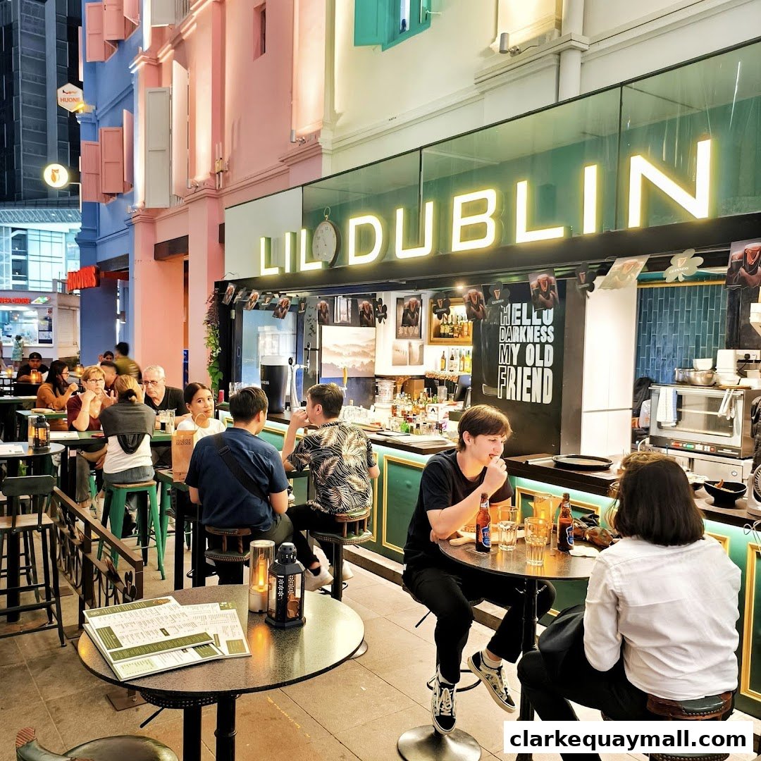 People enjoying drinks at outdoor tables in front of a bar with neon signage.