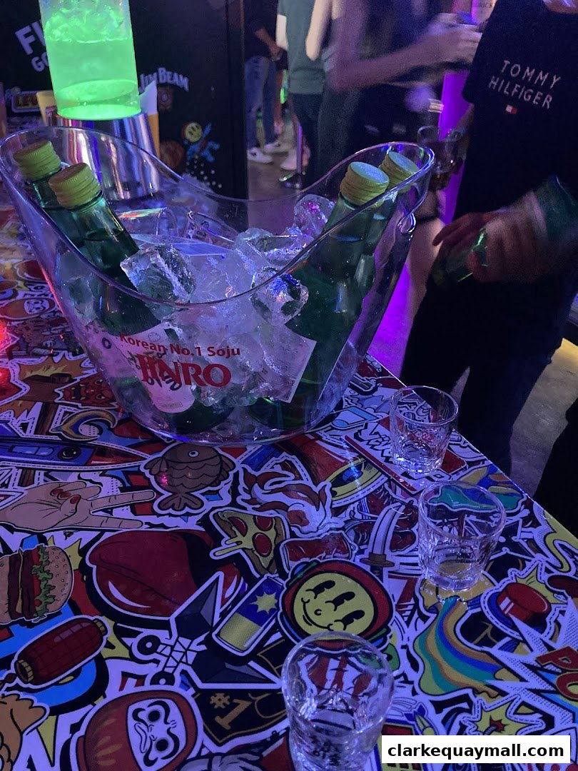 Bottles of Jinro Soju chilling in an ice bucket on a colorful, sticker-covered table.