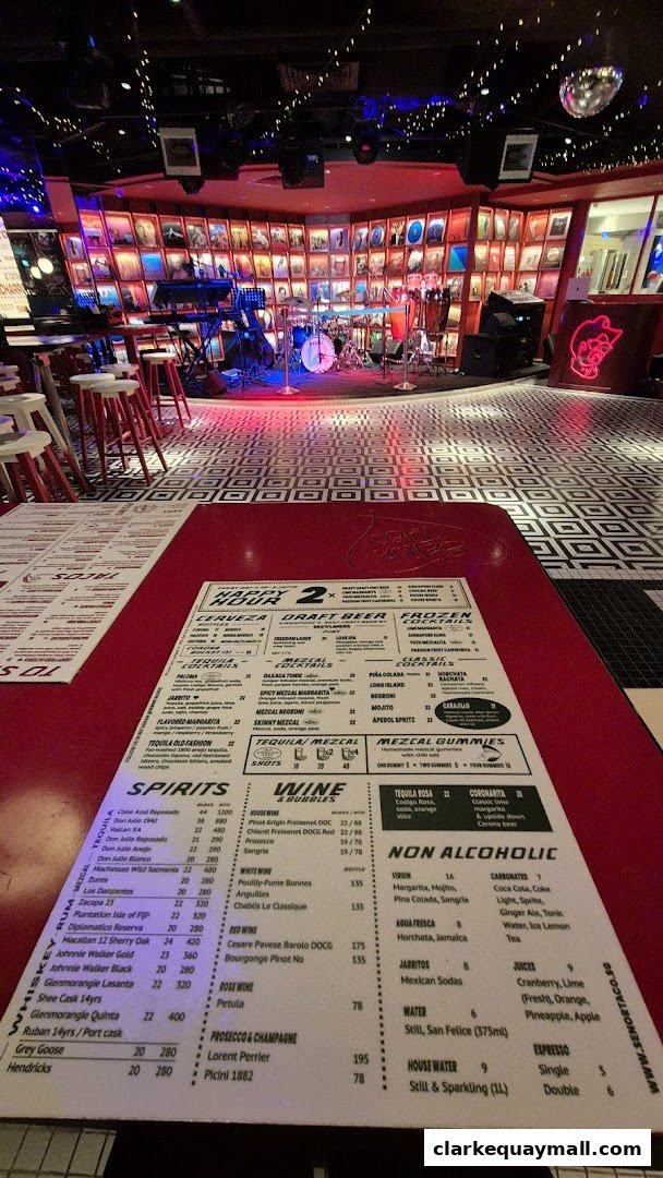A menu is laid out on a red table in front of a stage with musical instruments.