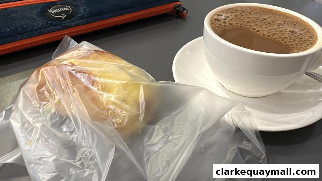 A pastry in plastic wrap next to a cup of coffee on a table.