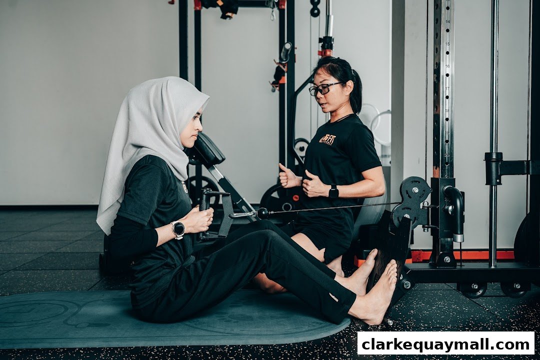 A trainer guides a client performing a seated row exercise on a cable machine.