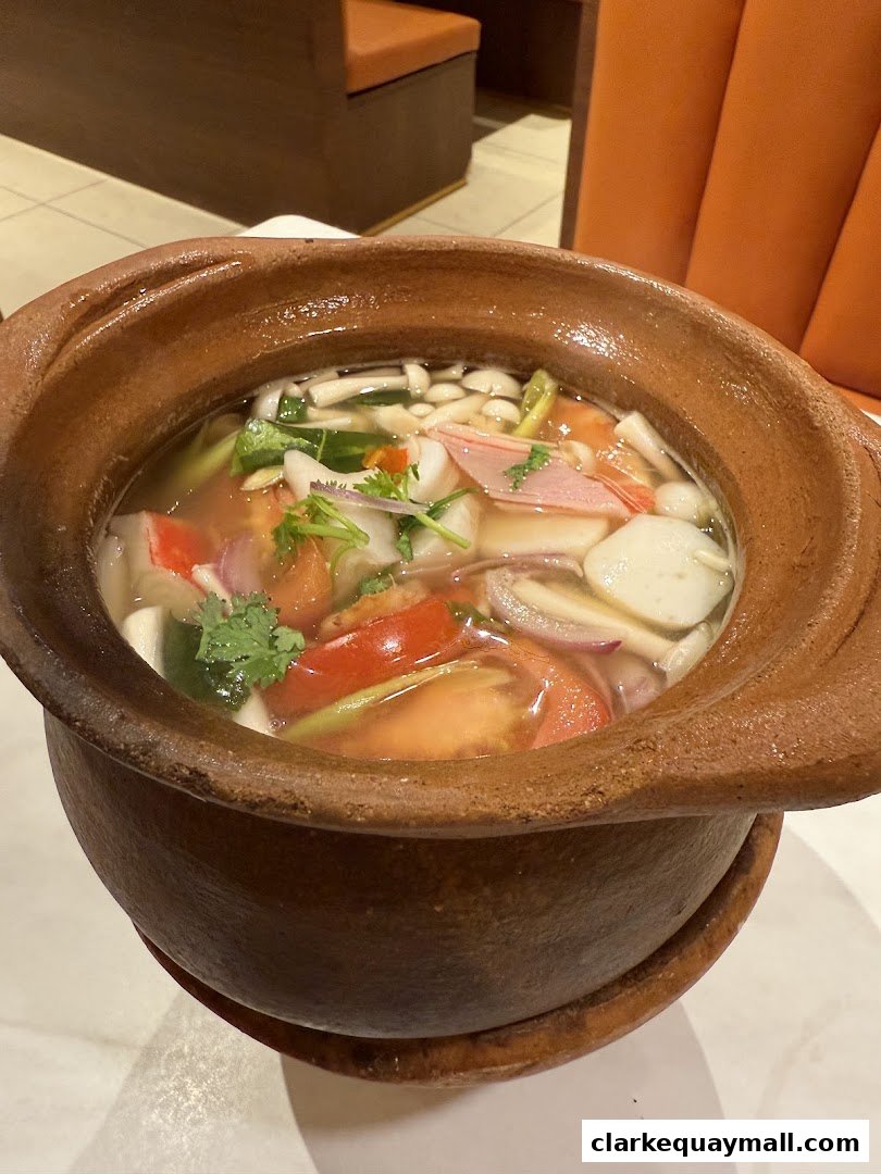A close-up of a steaming clay pot filled with a flavorful Thai soup, featuring seafood and vegetables.