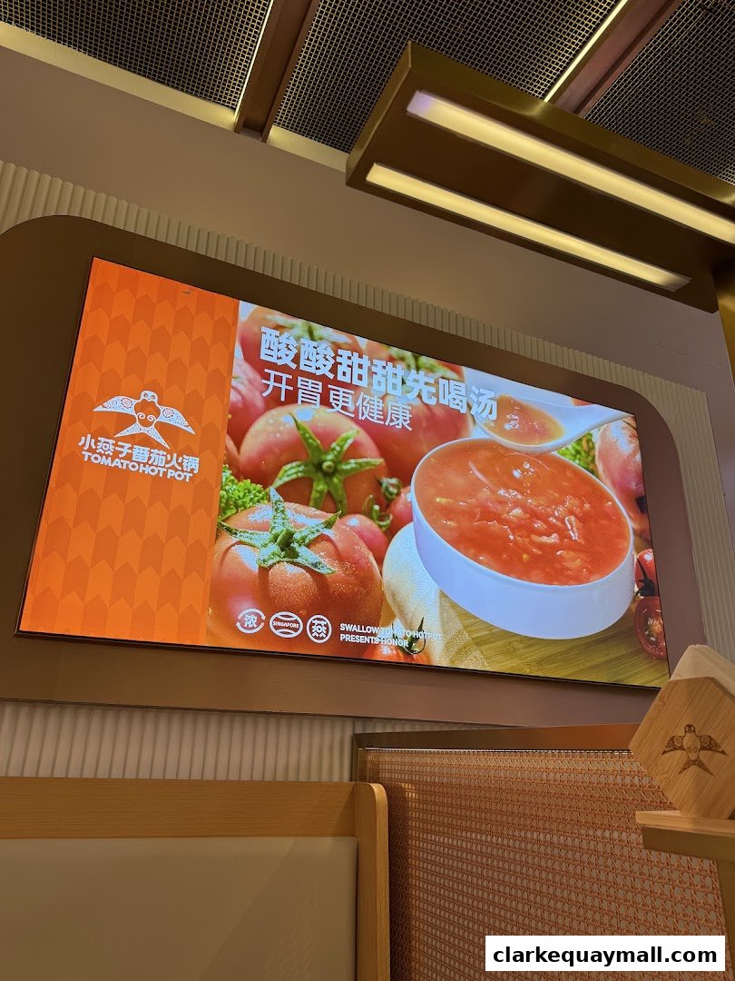 A digital screen displays a vibrant image of tomatoes and tomato soup, advertising XiaoYanZi Tomato Hot Pot.