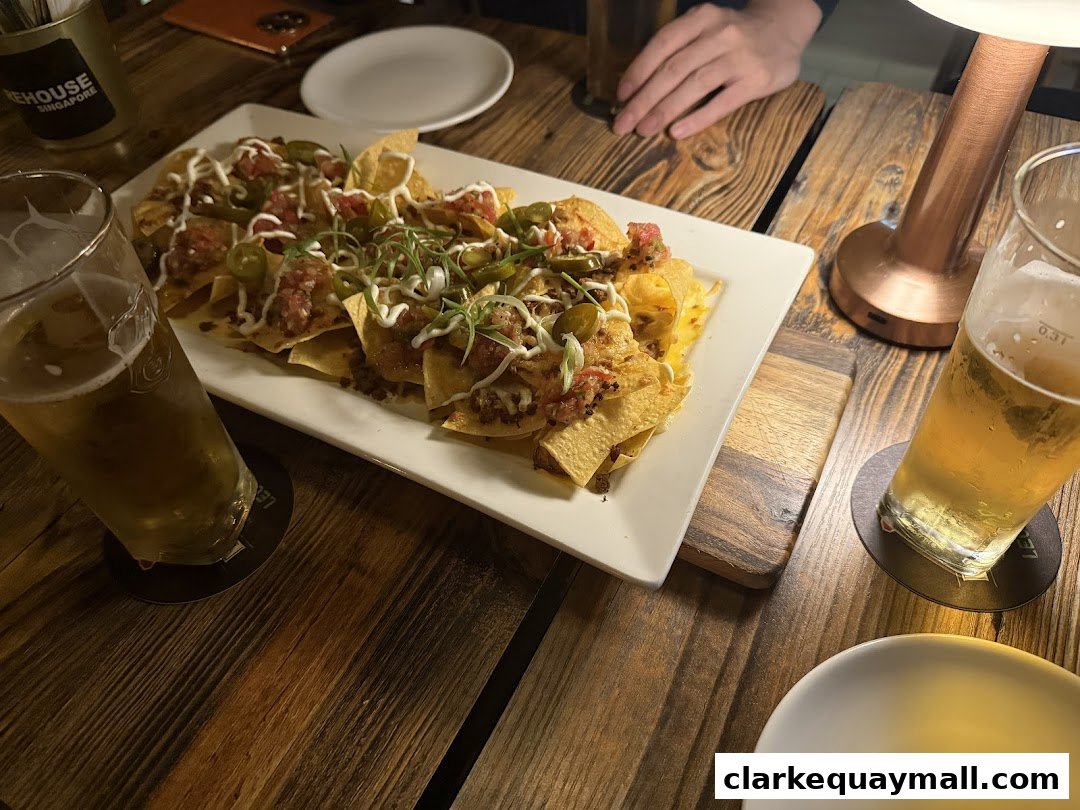 A plate of loaded nachos and two glasses of beer on a wooden table.