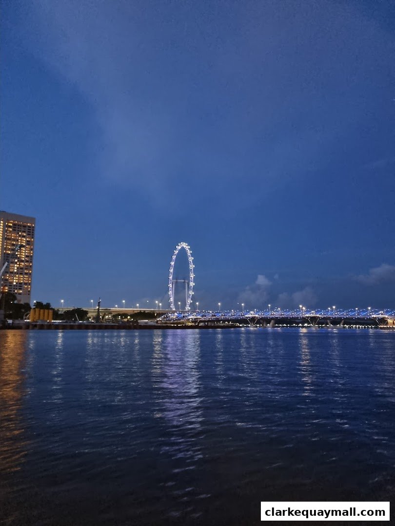 A scenic view of a river at dusk with a Ferris wheel and illuminated bridge in the background.