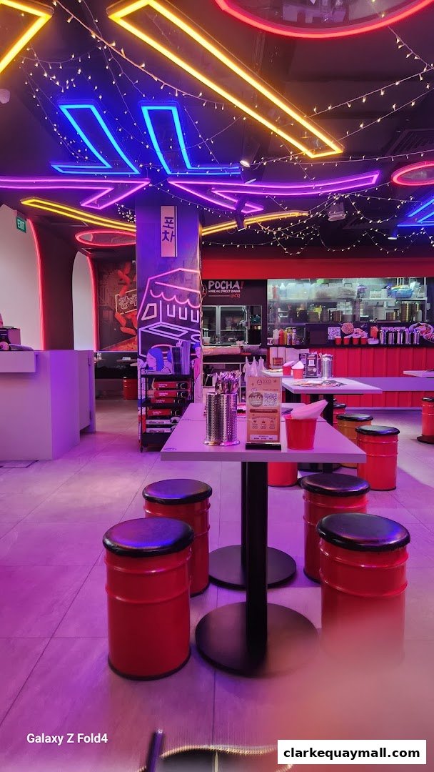 Interior of a Korean street dining restaurant with neon lights and red barrel stools.