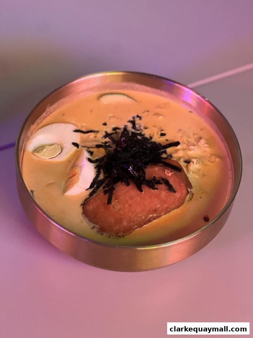 A close-up shot of a Korean dish in a metallic bowl, featuring noodles, egg, and meat.