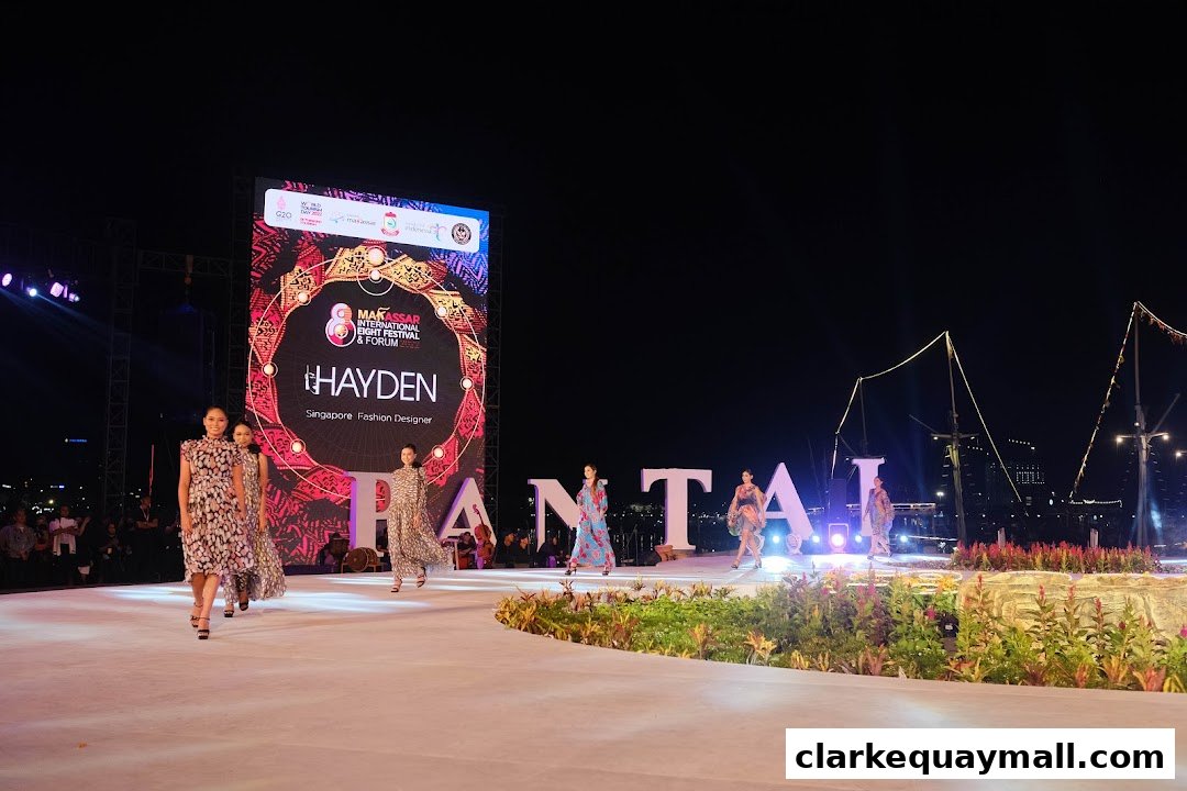 Models walk a runway at night in front of a large screen displaying "HAYDEN Singapore Fashion Designer".
